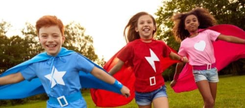 Carefree diverse superhero children running along meadow