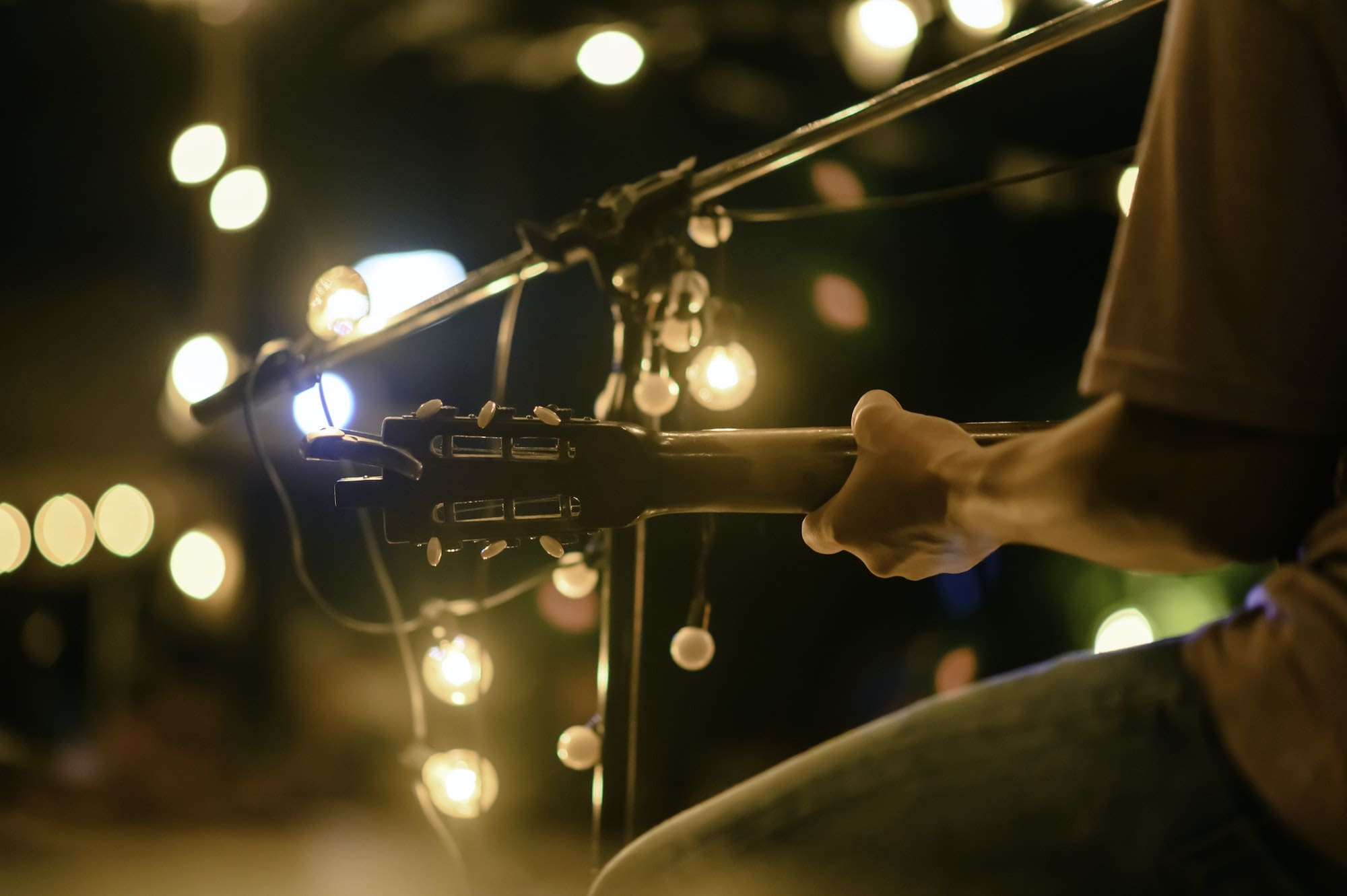 Rear view of the man sitting play acoustic guitar on the outdoor concert with a microphone